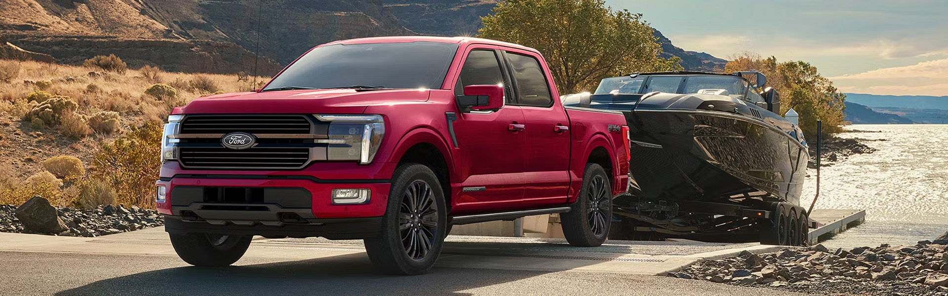 Red Ford F-150 towing a black boat on a lakeside boat ramp