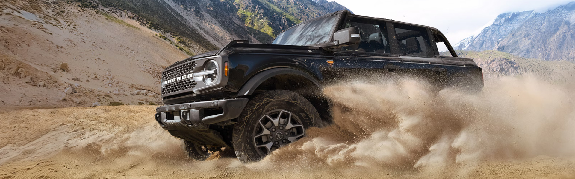 Black Ford Bronco driving through dust.